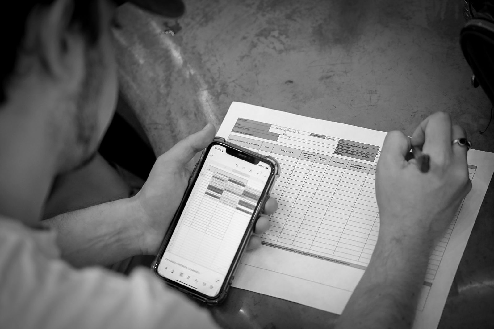 Manos sosteniendo un teléfono con el formulario de relevamiento y una planilla de seguimiento en papel.